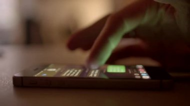Hafif ışıklandırılmış arka planda akıllı bir telefonla ustalıkla etkileşen bir elin yakın plan görüntüsü