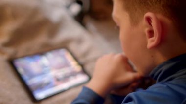 Bir çocuk evde rahatça dinlenirken dijital içeriği keşfetmek için tabletle meşgul.