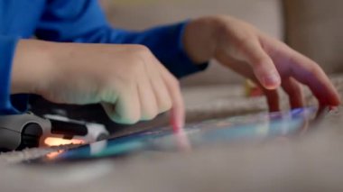 Bir çocuk, yastıklarla çevrili rahat bir koltukta tablet ve kumandayla mutlu bir şekilde oynar.