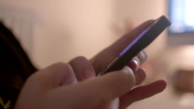 Bir kişi, hafifçe aydınlatılmış bir iç fonda otururken aktif olarak akıllı telefon kullanıyor.