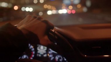 Gece direksiyonu sıkıca kavrayan bir el, arka planda bir şehir yolu ve gösterge paneli var.