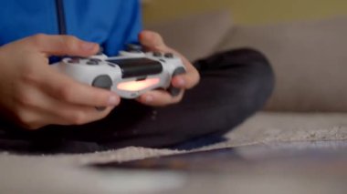 Kapalı bir ortamda rahat bir şekilde oturan bir çocuk dikkatle oyun kontrolörüyle oynamaya odaklanır.