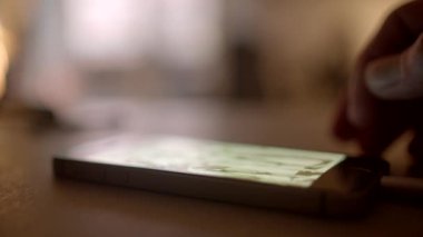 Arka plan bulanık görünürken bir el masanın üzerine yerleştirilmiş akıllı telefona uzanıyor.