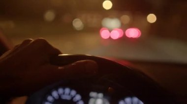 Gece araba sürerken direksiyona sıkıca tutunan bir el. Arka planda ışıklar bulanık.