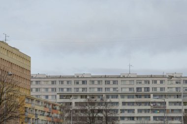 Şehrin bulutlu ve bulutlu bir gününde, sayısız penceresiyle karakterize edilen çok büyük bir bina diğer yapılarla çevrilidir.