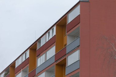 Mimari cazibesini ve işlevselliğini artıran çok sayıda pencere ve balkona sahip çarpıcı kırmızı bir bina gururla duruyor.