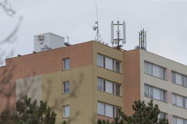 Tepesinde belirgin antenler bulunan yüksek bir bina, aşağıdaki canlı kentsel alanın ufuk çizgisine hakim.