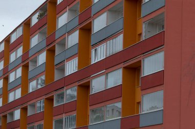 Bir apartman dairesi, alanı doğal ışıkla dolduran sayısız pencerenin yer aldığı canlı kırmızı ve turuncu renkte boyanmış.