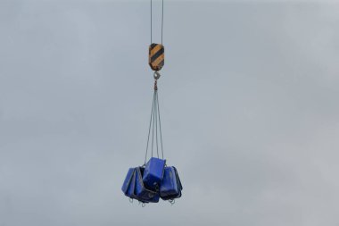 Büyük bir vinç, mavi bir nesneyi havaya kaldırıyor ve bu da güçlü yeteneklerini, hassasiyetini ve istikrarını gösteriyor.