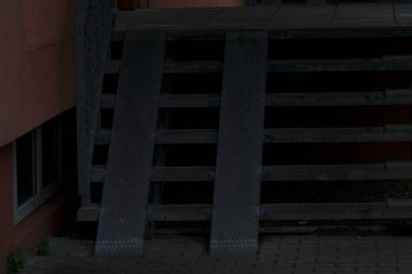 Gecenin karanlığında, ahşap bir merdiven binanın tam önüne yerleştirilir ve ayak seslerini bekleyen uzun gölgeler bırakır.