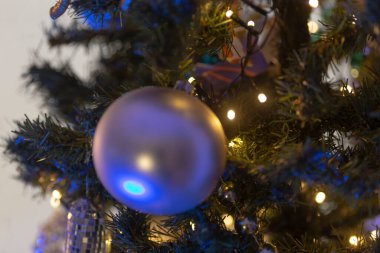 Dallarından sarkan parlak mavi bir süs topuyla süslenmiş güzel dekore edilmiş bir Noel ağacının detaylı bir yakın çekimi.