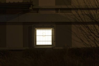 Binanın kenarında, gecenin karanlığında güzel bir şekilde parlayan bir pencere, çevresiyle çarpıcı bir kontrast oluşturuyor.