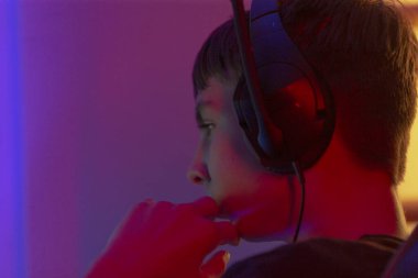 Şık kulaklıklar takan genç bir çocuk son derece odaklanmış ve konsolunda heyecan verici bir video oyunu oynamaktan hoşlanıyor.