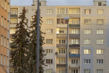 Kentsel bir apartman dairesi, alacakaranlık saatinde aydınlatılmış pencereleri arka plan olarak sunar