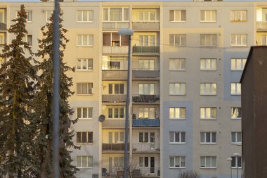 Bir konut binasının güneşli balkonları ve gür ağaçları olan güzel bir cephesi vardır.