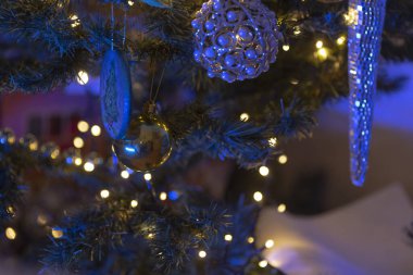 This image showcases a closeup view of a beautifully adorned Christmas tree, featuring vibrant blue lights and an assortment of colorful decorations clipart