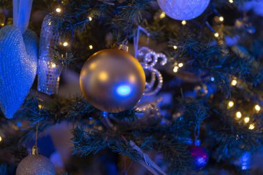 Göz kamaştırıcı mavi ışıklar ve çeşitli dekorasyonlarla süslenmiş parlak ışıklandırılmış bir Noel ağacının güzel yakın çekim görüntüsü.