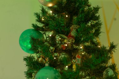 Canlı yeşil süslemelerle süslenmiş güzel dekore edilmiş bir Noel ağacının detaylı yakın plan görüntüsü şenlikli bir atmosfer yaratıyor.