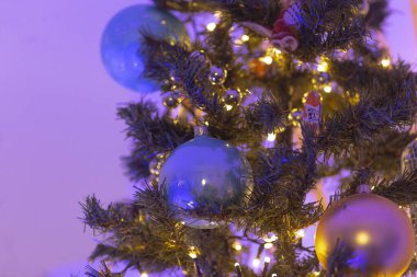 Bu, mavi ve altın süslerle süslenmiş güzel dekore edilmiş bir Noel ağacının yanı sıra yanıp sönen ışıkların yer aldığı yakın çekim görüntüsü.