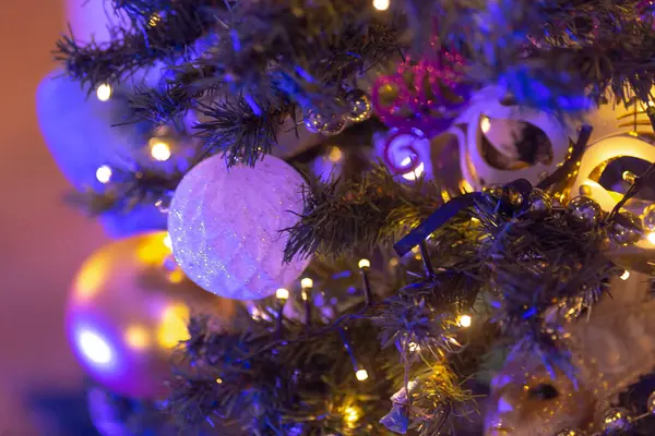 Bu görüntü, canlı mor ve parlak sarı ışıklar ve çeşitli süslerle süslenmiş güzel dekore edilmiş bir Noel ağacının yakın plan görüntüsünü yakalıyor.