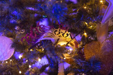 A beautifully adorned Christmas tree with a festive mask hanging from its branches, creating a unique holiday atmosphere clipart