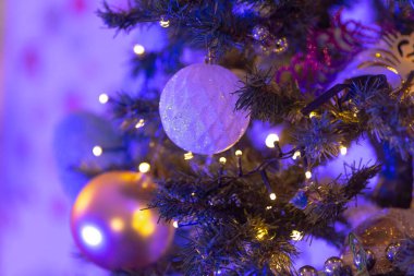 Bu resim, canlı mor ışıklar ve çeşitli süslerle süslenmiş güzel dekore edilmiş bir Noel ağacının yakın görüntüsünü içeriyor.