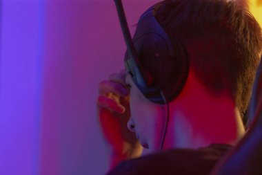 Bir adam oyun konsolunda oyun oynarken kulaklık ve mikrofon takarken rahat bir şekilde oturuyor.