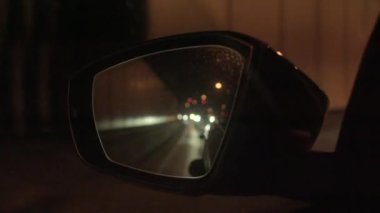 Araç ışıkları, karanlık bir tünelde seyahat ederken yan aynaya yansıyor ve şehir içi ulaşımı gösteriyor.