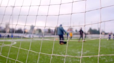 Futbolcular arka planda antrenman yaparken futbolcular geniş bir alanda aktif olarak antrenman yapıyorlar ve arka planda net bir hedef net olarak görülüyor.