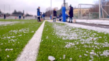 Futbol sahasının hemen dışında futbol antrenmanı, buzun yer yüzeyine saçıldığı bir çim sahasında yapılıyor.