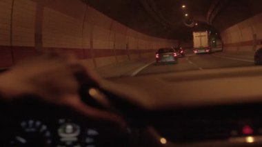 Parlak bir gösterge paneli, hareketli bir trafik ve aydınlatılmış bir şehir arkaplanı olan bir gece tüneli sahnesi.