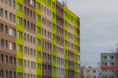 Konut binası yeşil ve kahverengi panellere sahiptir ve kentsel bir ortamda çağdaş mimariyi sergiler.