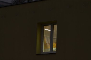 Koyu sarı bir arka planda yer alan parlak ışıklı bir pencere, geceleri çarpıcı bir şekilde öne çıkar.