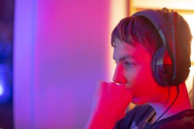 Genç bir oyuncu oyuna dalmış, kulaklık takıyor, parlak, renkli bir arka planı var.