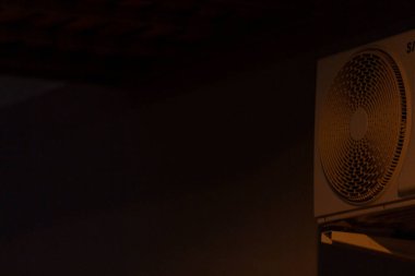 Loş bir odanın arka planında, duvara monte edilmiş bir klima var.