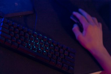 Bir el, karanlık bir yüzeye yerleştirilmiş aydınlanmış bir klavyenin yanındaki bilgisayar faresinin üzerinde duruyor.