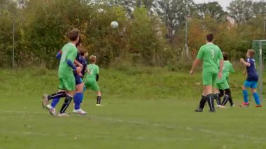 Çimenli bir sahada heyecan verici bir açık hava maçı sırasında yeşil ve mavi giyinmiş genç futbolcular birbirlerine karşı şiddetle yarışıyor, yetenek ve atletizm CZ, Kralupy, 12.10.24