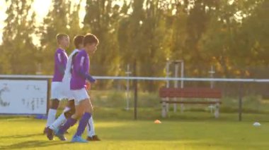 Genç futbolcular bir sahada enerjik bir şekilde mücadele ediyor, CZ, Kladno, 18.10.24 gün batımı altında yetenek ve takım çalışması sergiliyorlar.