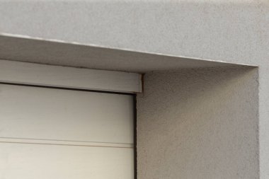 Bu resim, el değmemiş beyaz bir garaj kapısının iki element arasındaki zıtlığı vurgulayan, dokulu gri bir duvara yakın çekim görüntüsünü içeriyor.