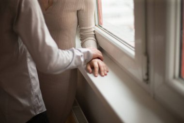 Bir çift elleri nazikçe ve sevgi dolu bir şekilde pencerenin kenarına dokunur. Kapalı bir arka planla çevrili.