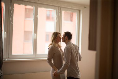 Arka planda güzel bir şehir arka planına sahip pencerenin yanında şefkatli bir öpücük paylaşan bir çift.