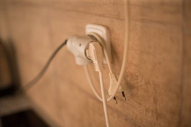 Üç elektrik kablosu tek bir prize takılır, kırsal ahşap bir duvar zeminine kurulur.