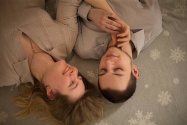 Bir çift, kar tanesi desenli bir arka planda yan yana yatarak bir anı paylaşıyor..