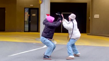 İki genç, neşeli bir şekilde canlı, renkli bir şehir zemininin önünde çömeliyor.