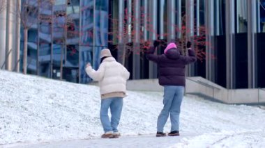 İki birey, karlı ve canlı bir şehir ortamının ortasında neşeli bir şekilde eğleniyorlar.