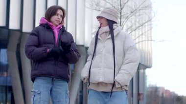 İki modaya uygun sokak giysisi giymiş canlı bir şehrin siluetine karşı sohbet ederek hareketli bir sahne yaratıyor.