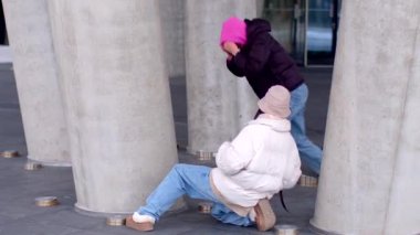 Canlı ve hareketli bir şehir ortamında, iki birey büyük beton sütunların yanında dinleniyor.