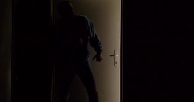 Esrarengiz bir figür karanlık ve gölgeli bir arkaplan karşısında bir kapıyı açarken görülebilir.