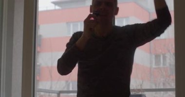 Bir adam dikkatle masaya eğiliyor ve şehir manzarası pencereden görülüyor.