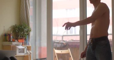 Genç bir adam, büyük bir pencereye yakın, parlak ve havadar bir odada güvenle duruyor.